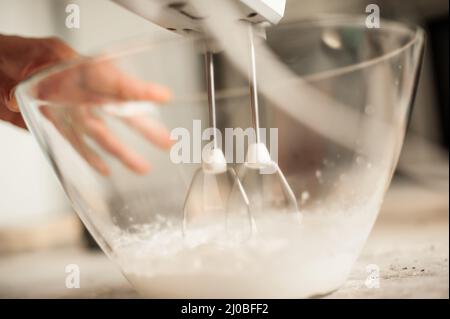 Frau hält den Mixer und macht Schlagsahne in einer Glasschüssel. Nahaufnahme Stockfoto