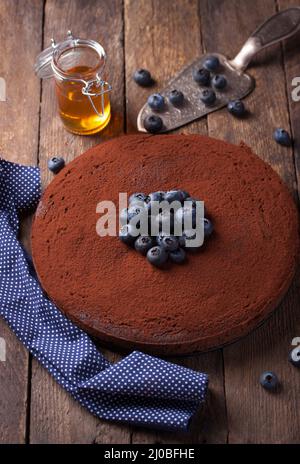 Schokoladenkuchen mit Kakaopulver und Heidelbeeren auf einem Holzhintergrund. Selektiver Fokus Stockfoto