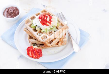 Waffeln mit Vollkornmehl und Früchten auf einem weißen Teller auf einer blauen Serviette Stockfoto