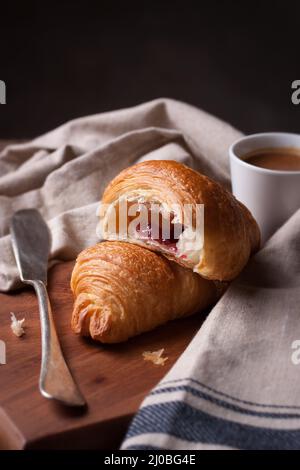 Nahaufnahme eines Croissants mit Marmelade und Kaffee auf einem Holzhintergrund Stockfoto