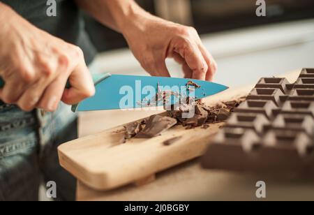 Nahaufnahme einer Frau, die die Hände hackt und den Schokoladenblock zum Festkuchen hackt Stockfoto