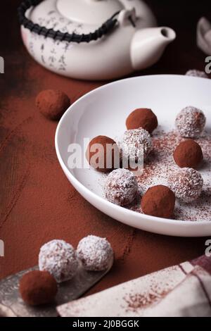 Schokoladenbonbons mit Kakao und Kokosnusschips auf einem weißen Teller Stockfoto