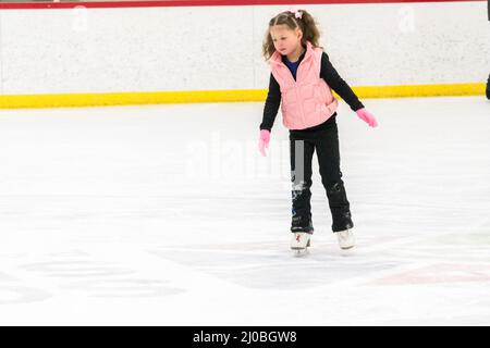 Kleine Mädchen, die Eiskunstlauf üben, bewegen sich auf der Indoor-Eisbahn. Stockfoto