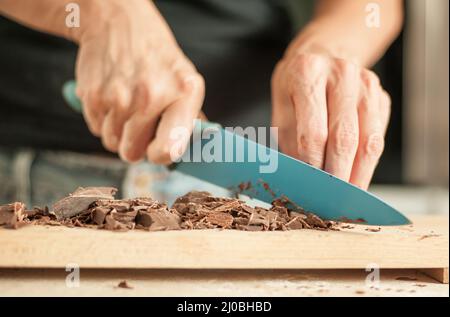 Nahaufnahme einer Frau, die die Hände hackt und den Schokoladenblock zum Festkuchen hackt Stockfoto