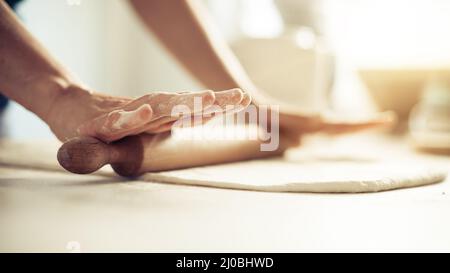 Frau, die Teig auf einem Holztisch mit Holzpfeifholz rollt. Nahaufnahme Stockfoto