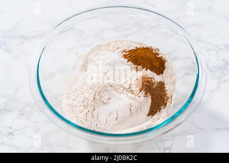 Mischen von trockenen Zutaten in einer großen Glasmischschüssel zum Backen von Eierkuchen mit einem Schokoladen-Lebkuchenmann. Stockfoto