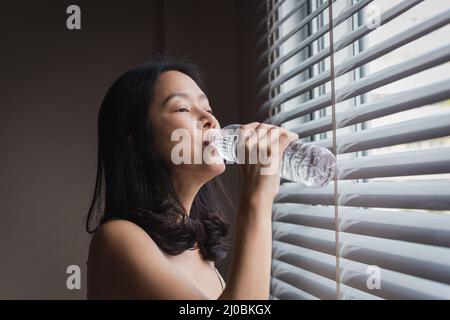 Frau trinkt Mineralwasser aus der Flasche nach dem Aufwachen im Schlafzimmer. Stockfoto