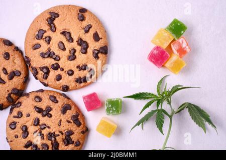 Amerikanische Cookies mit Cannabisextrakt. Süßigkeiten mit CBD-Öl. Marihuana Blätter auf weißem Hintergrund. Draufsicht, flach liegend. Stockfoto