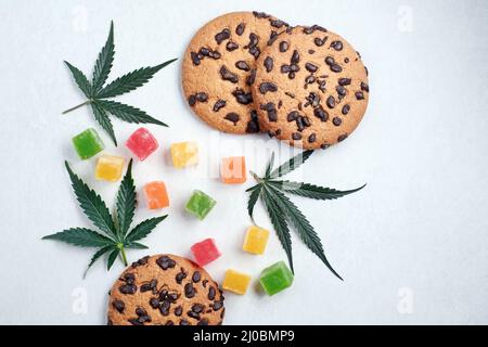 Marmelade und amerikanische Kekse mit Cannabisextrakt. Süßigkeiten mit CBD-Öl. Marihuana Blätter auf weißem Hintergrund. Draufsicht, flach liegend. Stockfoto