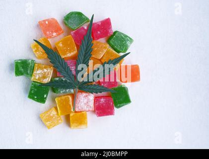 Layout von bunten Marmelade und Marihuana-Blatt auf weißem strukturiertem Hintergrund. Süßigkeiten mit CBD-Öl. Draufsicht, flach liegend. Stockfoto