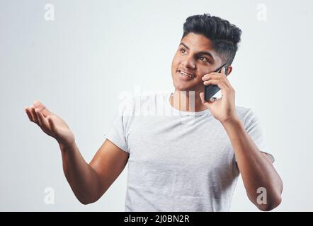 Lernen wir uns kennen. Studioaufnahme eines jungen Mannes, der auf seinem Handy spricht, während er vor einem weißen Hintergrund steht. Stockfoto