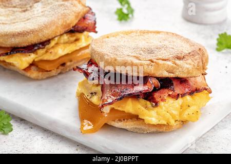Englisches Muffin, Ei, Schinken und Käse-Frühstückssandwich auf einem Schneidebrett Stockfoto