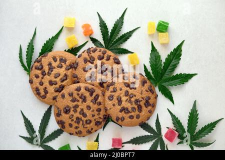 Amerikanische Cookies mit Cannabisextrakt. Süßigkeiten mit CBD-Öl. Marihuana Blätter auf weißem Hintergrund. Draufsicht, flach liegend. Stockfoto