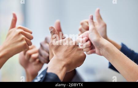 Wir lieben das, was Sie tun. Aufnahme einer Gruppe von Mitarbeitern, deren Arme in der Geste mit den Daumen nach oben angehoben wurden. Stockfoto