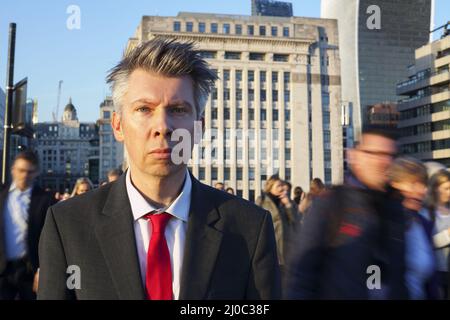 Geschäftsmann steht still, während die Leute hinter sich herlaufen Stockfoto