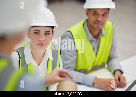 Dem Vorgesetzten zuhören. Aufnahme von zwei jungen Bauarbeitern aus der Baubranche, die einem Kollegen während einer Sitzung im Sitzungssaal zuhören. Stockfoto