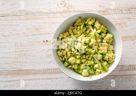 Zucchini in kleine Würfel geschnitten in einer weißen Schüssel auf einem hellen rustikalen Holztisch, gesundes Gemüse mit Mineralien und Vitaminen, aber kalorienarm, Kopie SPAC Stockfoto