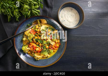 Hühnercury mit Kichererbsen und Gemüse, serviert mit Joghurt in blauen Schüsseln auf einem dunklen rustikalen Holztisch, Kopierraum, Blick von oben, s Stockfoto