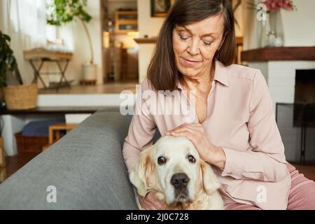 Die alte Frau streichelte ihren Hund zu Hause auf dem Sofa für Kameradschaft und Tierliebe Stockfoto