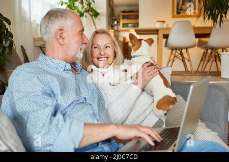 Rentnerpaar mit kleinem Hund, der zu Hause im Wohnzimmer einen Laptop benutzt Stockfoto