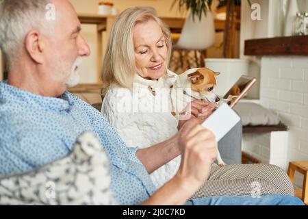 Rentnerehepaar mit Haustier Hund macht Online-Shopping zu Hause im Wohnzimmer Stockfoto