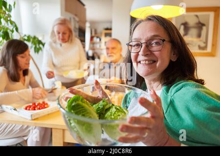 Eine ältere Frau hält eine Schüssel mit frischem Salat für einen gesunden Brunch mit Freunden in der Küche Stockfoto