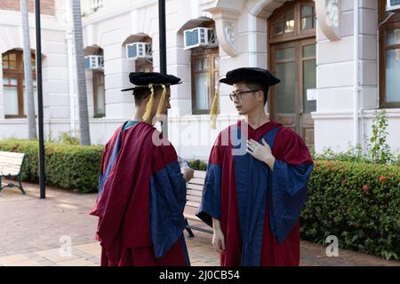 Zwei glückliche stolze Doktoranden graduierten in akademischem Kleid im Chat Stockfoto