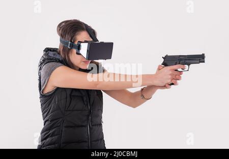 Frau spielen VR-Shooter-Spiel mit VR-Brille und Pistole. Studioaufnahmen Stockfoto