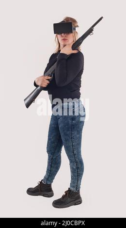 Frau spielen VR-Shooter-Spiel mit VR-Brille und Gewehr. Studioaufnahmen Stockfoto