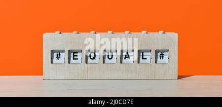 Das Wort gleich in einem rustikalen hölzernen Split Flap Board, auf einer hölzernen Oberfläche vor einem orangen Hintergrund, in einem Panorama-Format als Webbanner oder er zu verwenden Stockfoto
