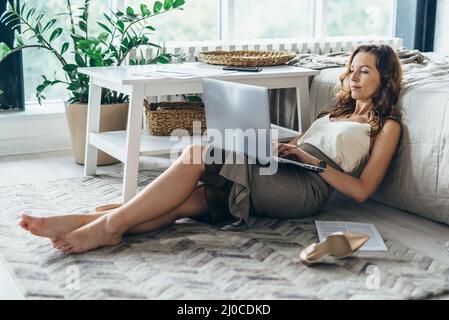 Junge Frau mit Laptop, während sie zu Hause im Schlafzimmer auf dem Boden liegt. Stockfoto