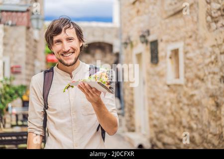 Junger Tourist, der traditionelle Pizza in der Altstadt von Budva isst. Reise nach Montenegro Konzept Stockfoto