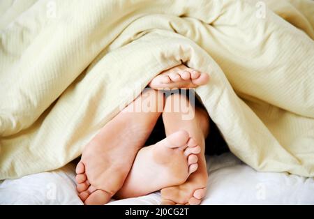 Intimität unter den Decken. Ein kurzer Schuss von den Füßen eines Paares, die unter der Bettwäsche herausstochen. Stockfoto