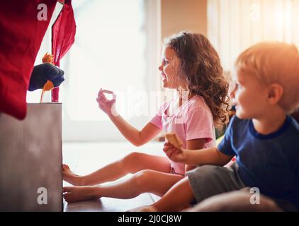 Eine Show zu zeigen. Aufnahme von zwei kleinen Geschwistern, die zu Hause ein Puppentheater anschauen. Stockfoto