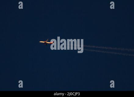 Ein kommerzielles Verkehrsflugzeug mit Kondensstreifen in großer Höhe fliegt bei Sonnenuntergang durch einen tiefblauen Himmel. Stockfoto