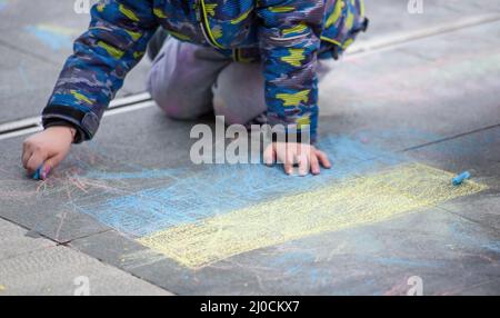 Das Kind zeichnet die blau-gelbe Flagge der Ukraine auf den Asphalt Stockfoto