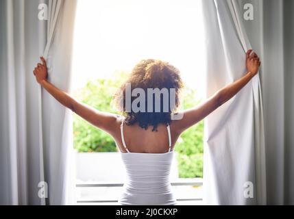 Guten Morgen Welt. Rückansicht einer unkenntlichen Frau, die ihre Vorhänge im Schlafzimmer öffnete, nachdem sie aus dem Schlaf aufgewacht war. Stockfoto