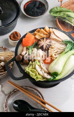 Sojamilch-Hot Pot-Rezept mit napa-Kohl, Pilzen und in dünne Scheiben geschnittenem Schweinefleisch, gekocht in einer cremigen und herzhaften Sojamilchbrühe. Stockfoto