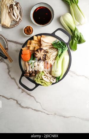 Sojamilch-Hot Pot-Rezept mit napa-Kohl, Pilzen und in dünne Scheiben geschnittenem Schweinefleisch, gekocht in einer cremigen und herzhaften Sojamilchbrühe. Stockfoto