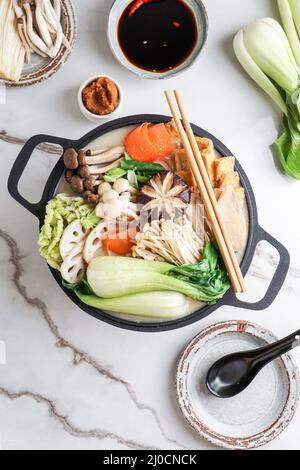 Sojamilch-Hot Pot-Rezept mit napa-Kohl, Pilzen und in dünne Scheiben geschnittenem Schweinefleisch, gekocht in einer cremigen und herzhaften Sojamilchbrühe. Stockfoto