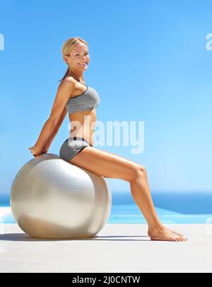 Gefühl und Aussehen erstaunlich. Porträt einer attraktiven jungen Frau, die mit einem Gymnastikball am Pool trainiert. Stockfoto