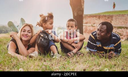Outdoor-Porträt einer glücklichen internationalen Familie, die Spaß hat und auf einem grünen Gras im Park liegt Stockfoto