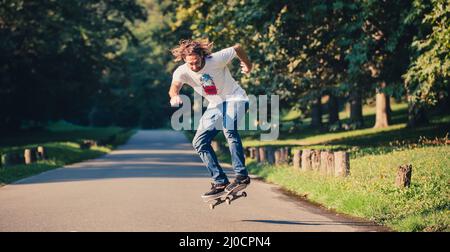 Action-Aufnahme eines Skateboarders beim Skaten, beim Kunststück und beim Springen auf der Straße durch den Wald. Freies Reiten Skateboard Stockfoto