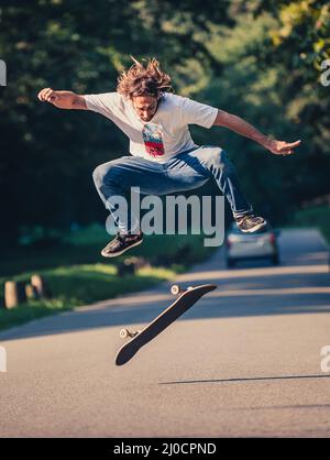 Action-Aufnahme eines Skateboarders beim Skaten, beim Kunststück und beim Springen auf der Straße durch den Wald. Freies Reiten Skateboard Stockfoto