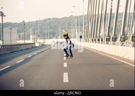 Skateboarder, die einen Skate fahren und Sprünge auf der Stadtstraßenbrücke machen, durch den Stadtverkehr. Free Ride Skateboards Stockfoto