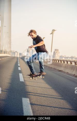 Skateboarder, die einen Skate fahren und Sprünge auf der Stadtstraßenbrücke machen, durch den Stadtverkehr. Free Ride Skateboards Stockfoto