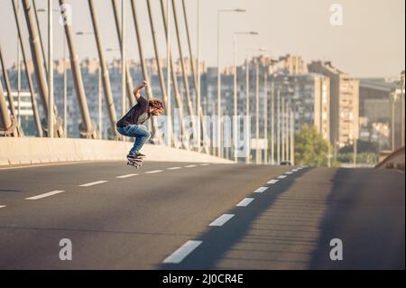 Skateboarder, die einen Skate fahren und Sprünge auf der Stadtstraßenbrücke machen, durch den Stadtverkehr. Free Ride Skateboards Stockfoto