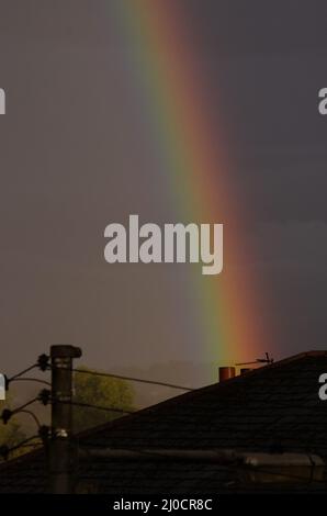 Regenbogen, der hinter Schornsteintöpfen auf einem Dach aufsteigt Stockfoto