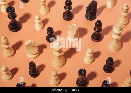 Verschiedene Schachfiguren, die zufällig auf einem orangefarbenen Hintergrund mit einem schattenverzerrten, hohen Winkel angeordnet sind Stockfoto