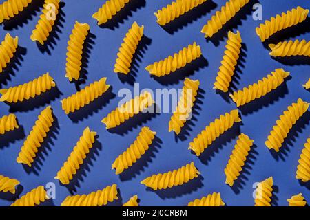 Getrocknete, spiralförmige italienische Pasta, die in einem Vollformat auf Blau gestreut ist, als flaches Stillleben angesehen Stockfoto